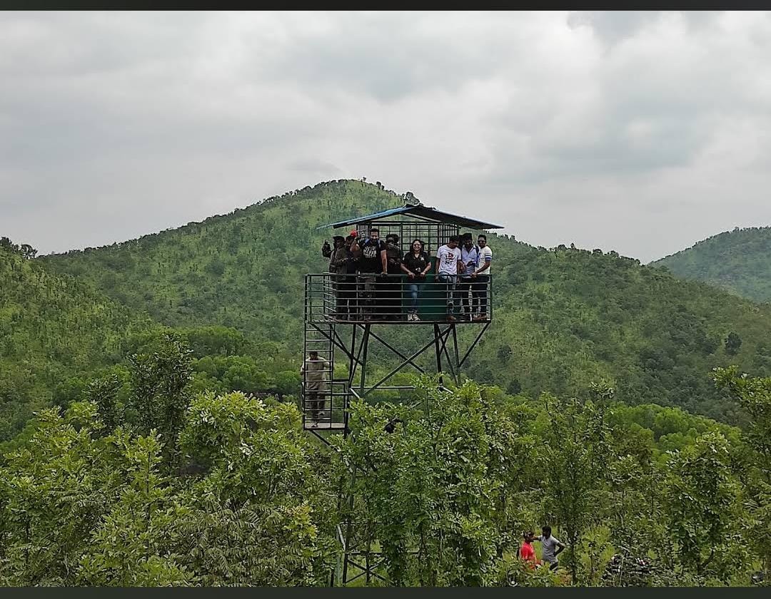 Group of people on a tall, metal observation tower with lush green hills and cloudy sky in the background.