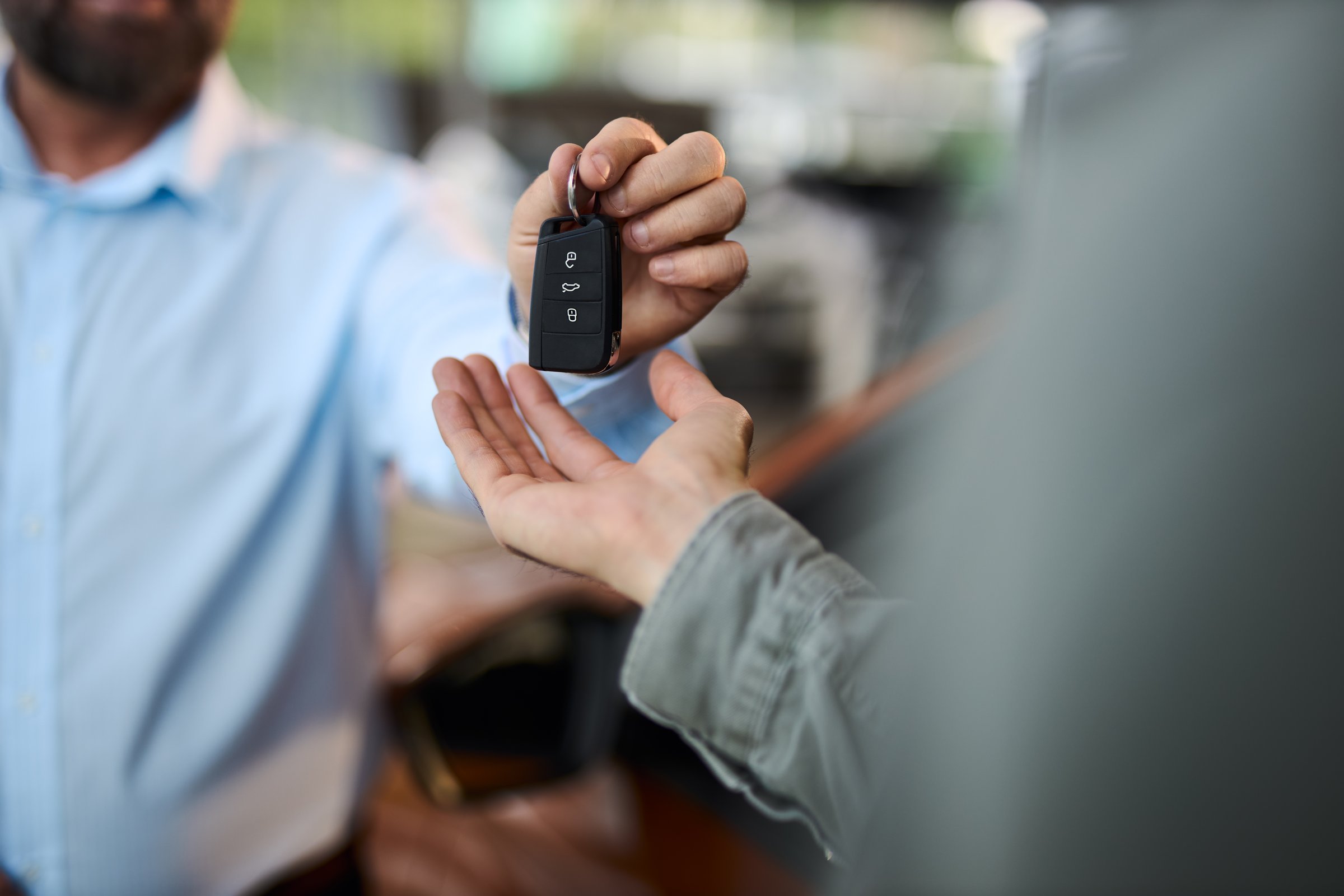 Close up of unrecognizable salesman giving car keys to his customer at a car dealership