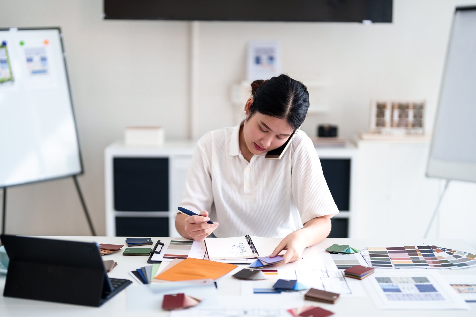 Interior designer making business call while working on color and material selection at design studio desk