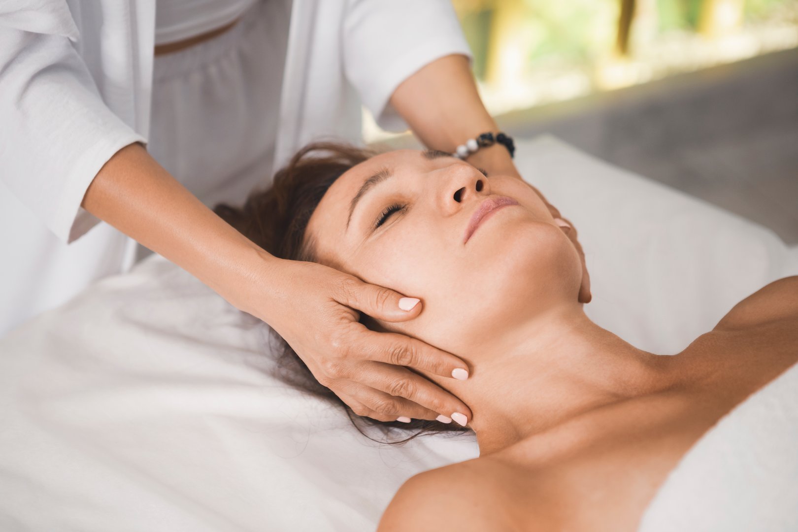 Therapists hands massage female head, close-up. Woman lying on back in pro salon, selective focus. Therapy, recovery, osteopathy, body care, face lifting, treatment concept.