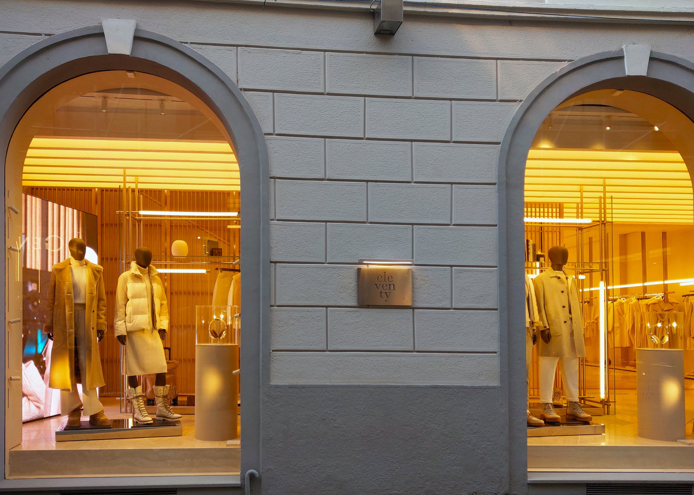 Milan, Italy, December 2, 2024: Storefront showcases two stylish mannequins dressed in chic, modern outfits under warm, ambient lighting. the arched windows and sleek store design emphasize sophistication and contemporary retail fashion trends.