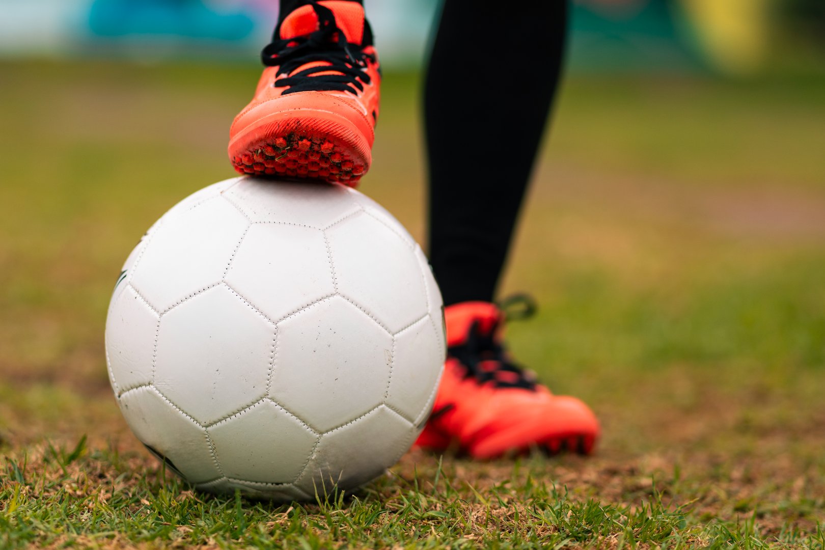 View of legs of brunette female soccer player running to kick soccer ball. on a green grass outdoors, with colorful background. with sports clothing. sports and wellness advertising