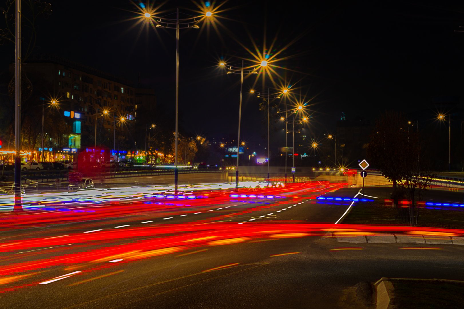 Night photography with a long exposure of a multi-lane road with an exit on which many cars are moving and leaving lines from the headlights and lights of marker and brake. Evening traffic jams.