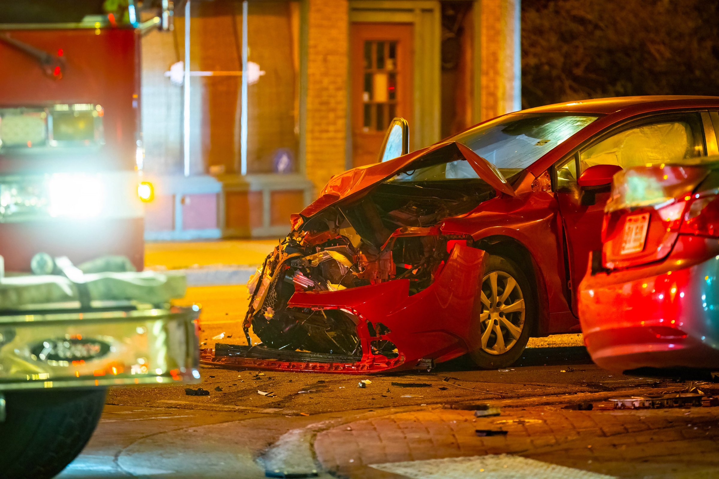 Nighttime scene showing a serious collision between two cars on a city street with visible damage, debris, and emergency atmosphere under streetlights.