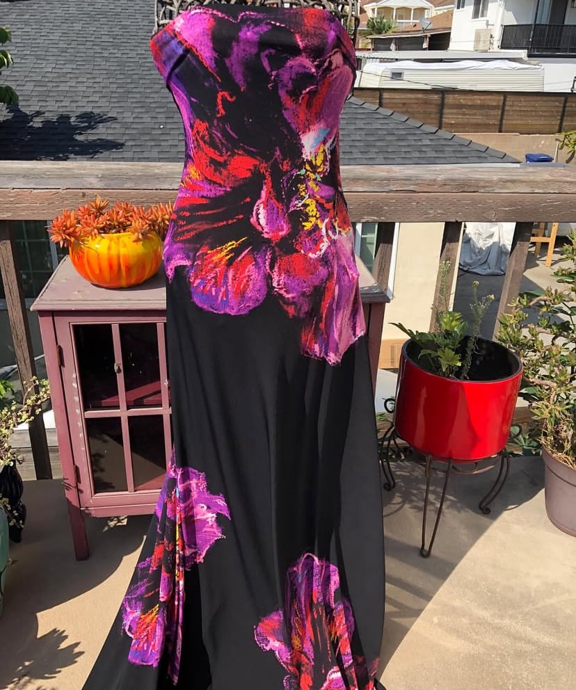 Strapless dress on a mannequin, featuring vibrant pink and purple floral patterns, displayed on a sunlit balcony.