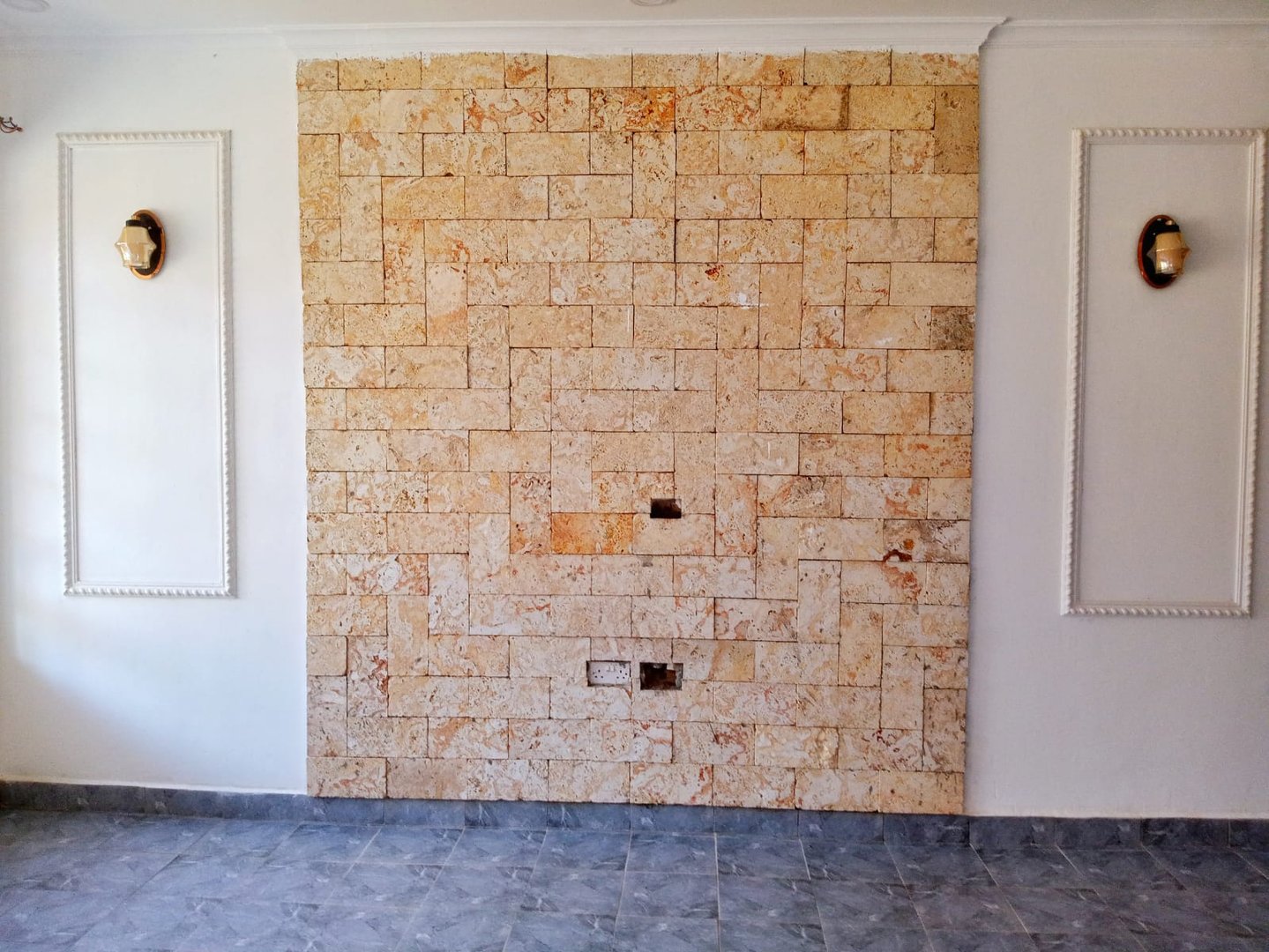 Room with a stone accent wall, two built-in light fixtures, and gray tiled flooring.