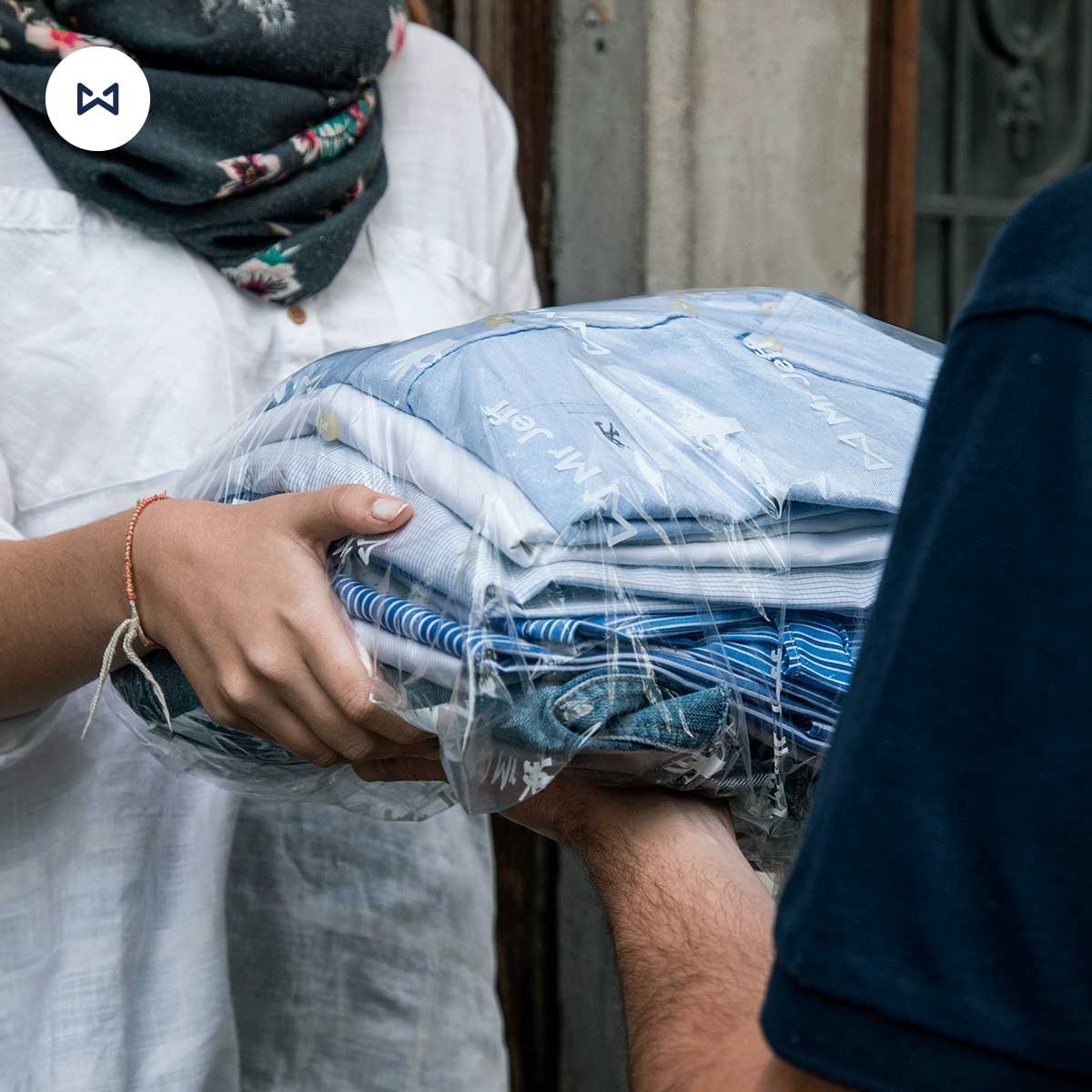 Two people exchanging a bundle of folded clothes wrapped in clear plastic.