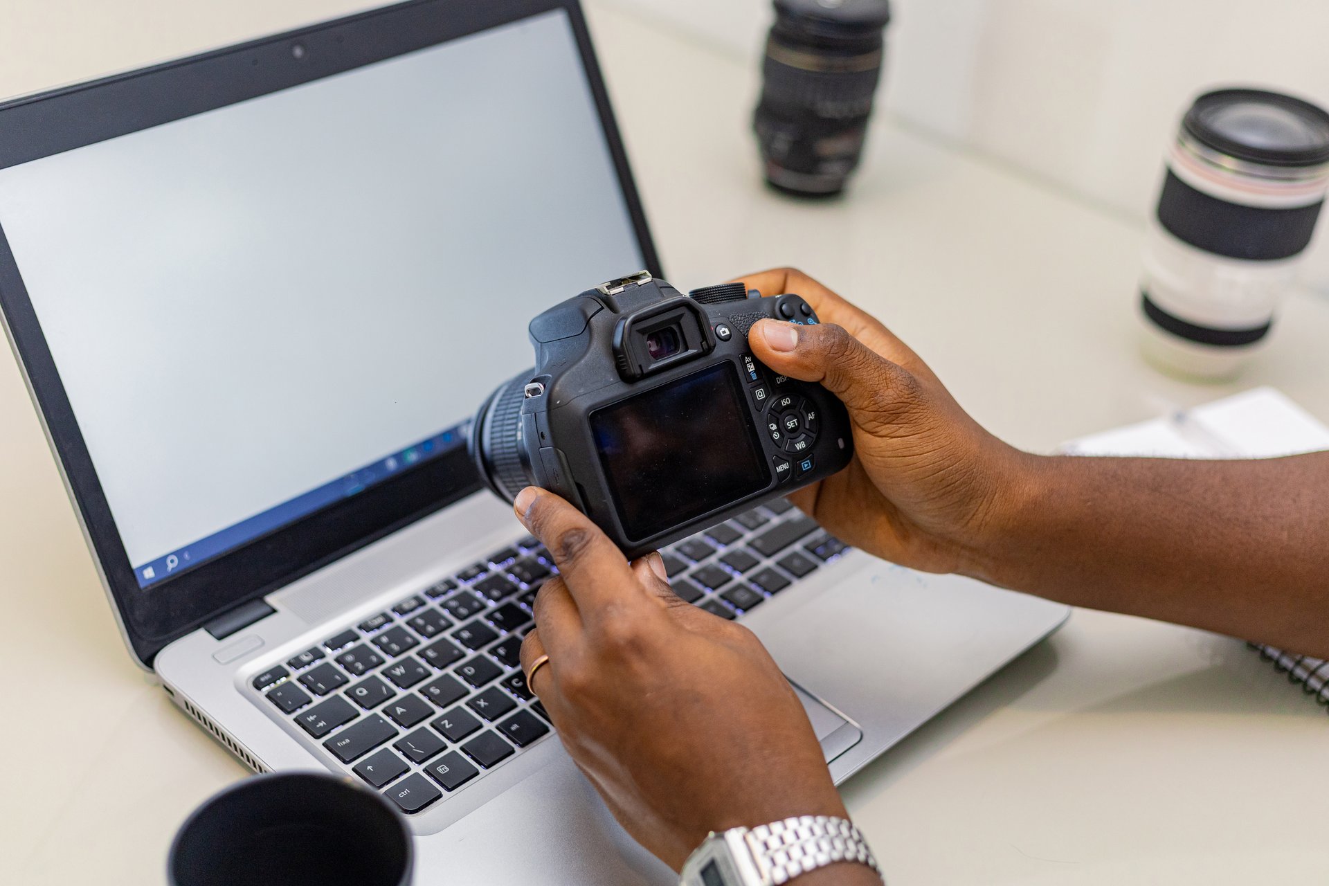 Photographer working with laptop and digital camera. Professional journalist or freelancer using notebook with DSLR camera and photography equipment on table.