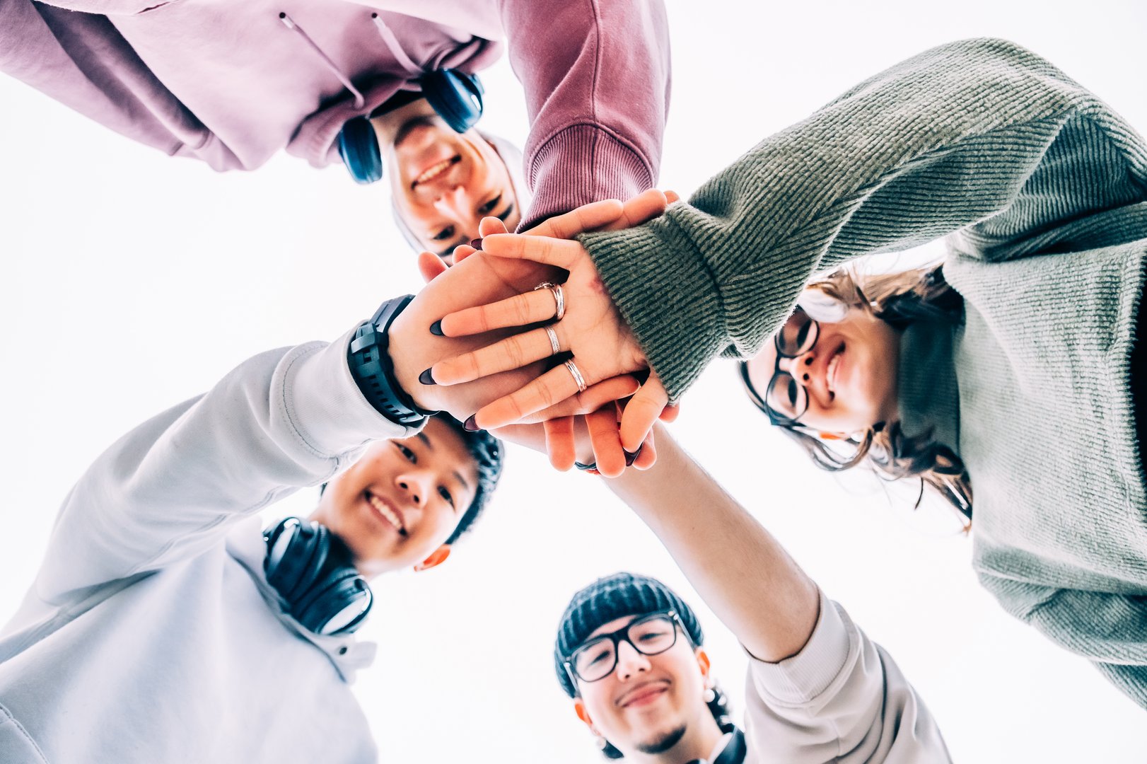 Four cheerful multi-ethnic students are putting their hands together, forming a circle, showing unity and teamwork, celebrating their friendship and cultural diversity