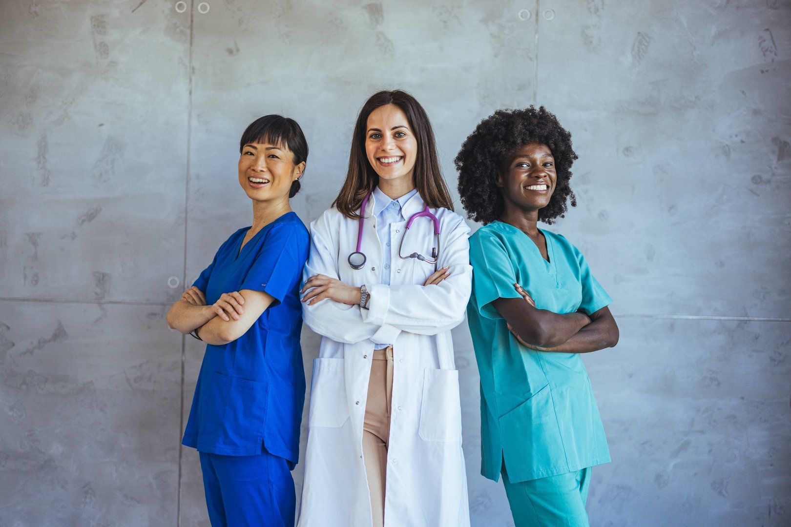 Diverse group of female healthcare professionals in scrubs and lab coat standing confidently with arms crossed, representing teamwork, diversity, and strength in the medical field.