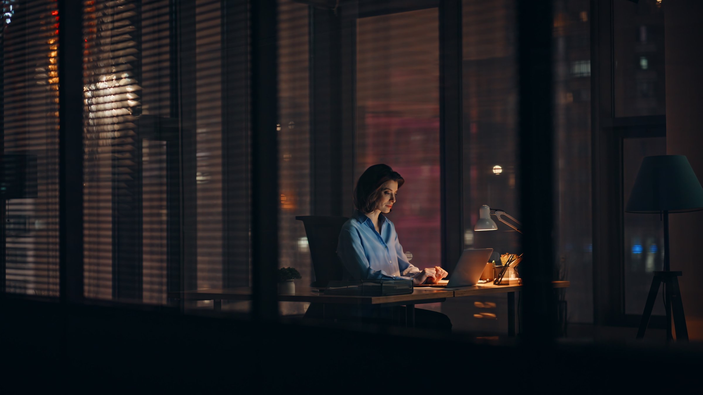 Night employee working on startup at dark corporate office. Hardworking businesswoman busy of overtime project looking laptop in lamp light. Elegant woman worker browse computer making deadline job.
