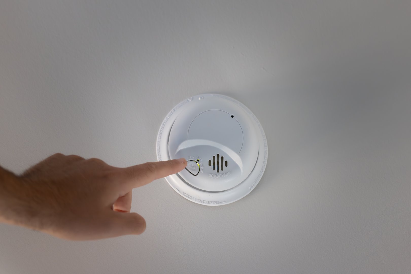 man pressing the test button on ceiling-mounted smoke and carbon monoxide detector