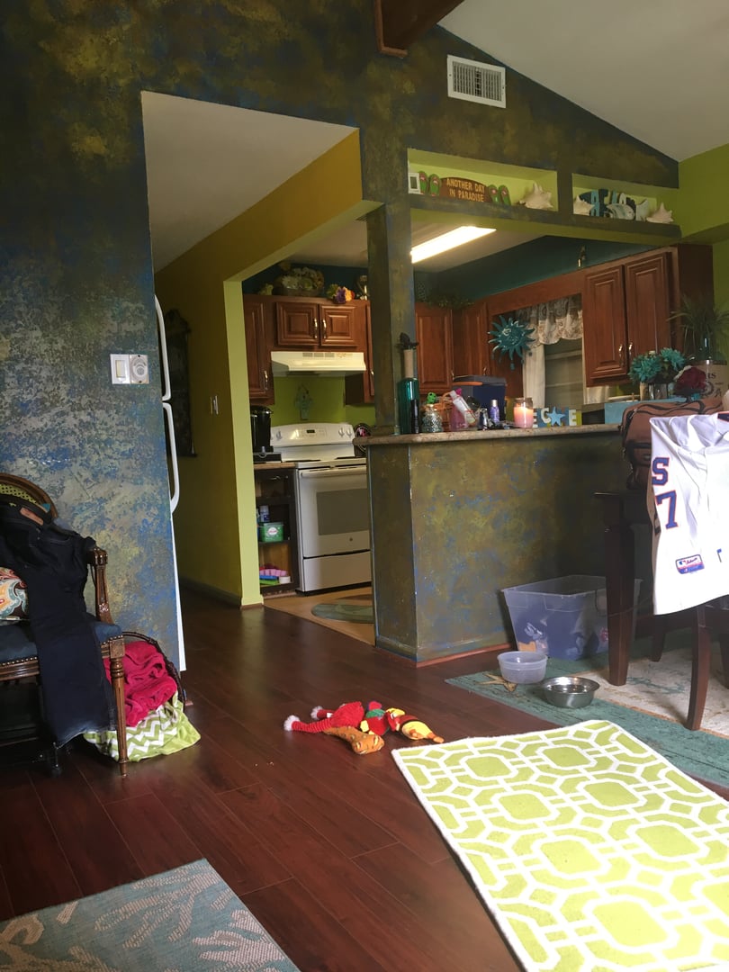 Colorful kitchen and dining area with wooden cabinets, painted walls, and scattered toys on the floor.