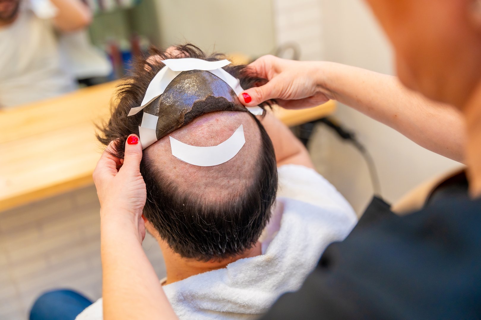 Top view close-up of a hairstylist attaching a wig to a man using adhesive stripes