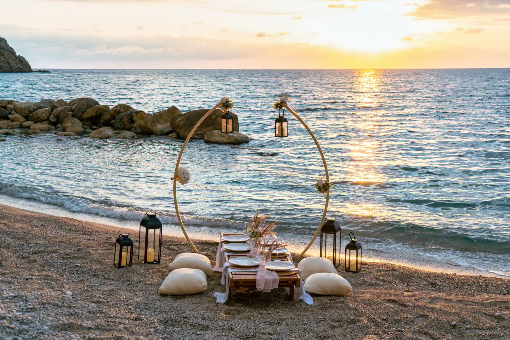 A romantic beachside table with ocean waves and a golden sunset view.