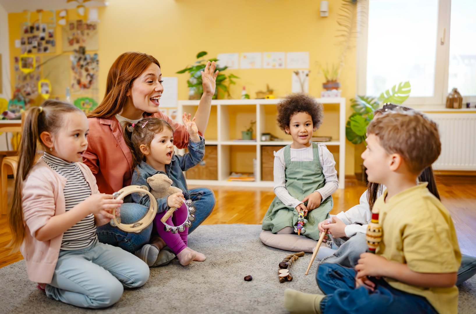 Multicultural group of preschool children playing musical instruments with a kindergarten teacher during a fun music activity in a bright, cheerful classroom