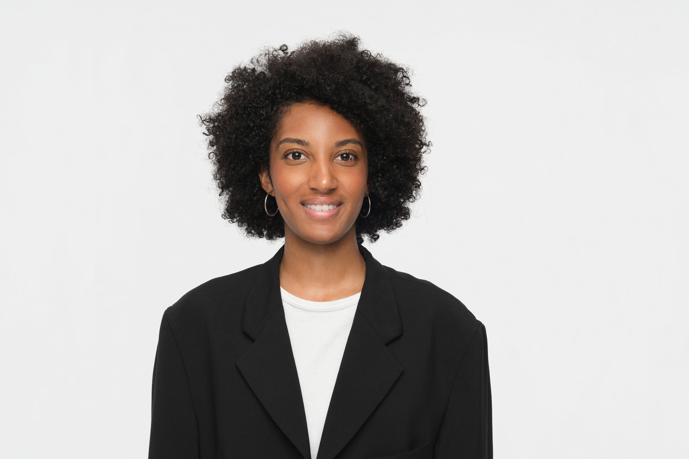 Confident woman wearing professional attire, smiling warmly while standing against a simple backdrop, radiating positivity and professionalism.