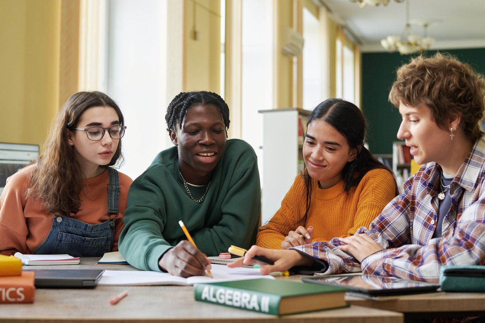 Group of students working on an algebra project in classroom setting, engaging in collaborative learning while sitting around table and sharing ideas on assignment