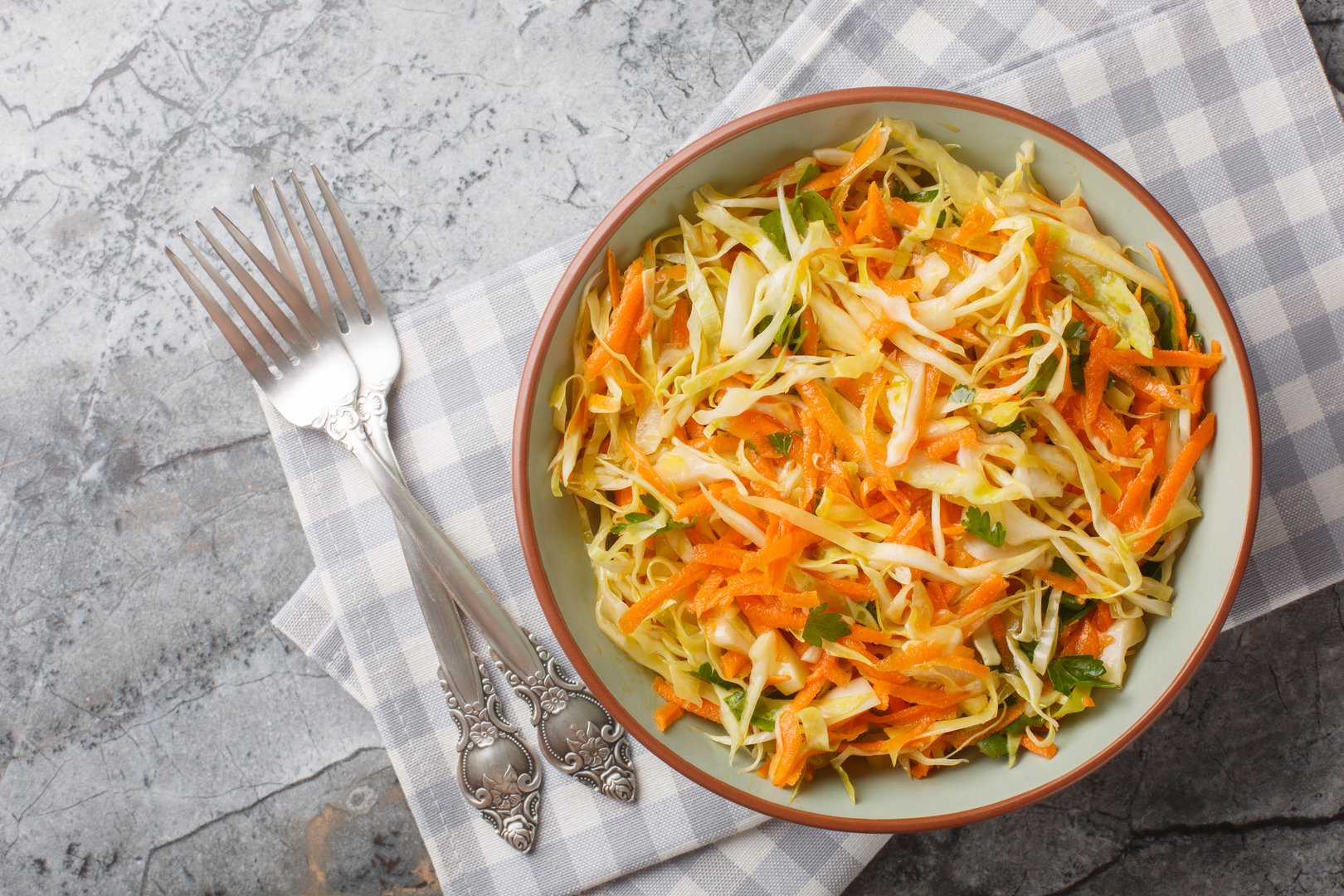 simple homemade salad of white cabbage with carrots seasoned with vinegar and olive oil close-up in a bowl on the table. Horizontal top view from above