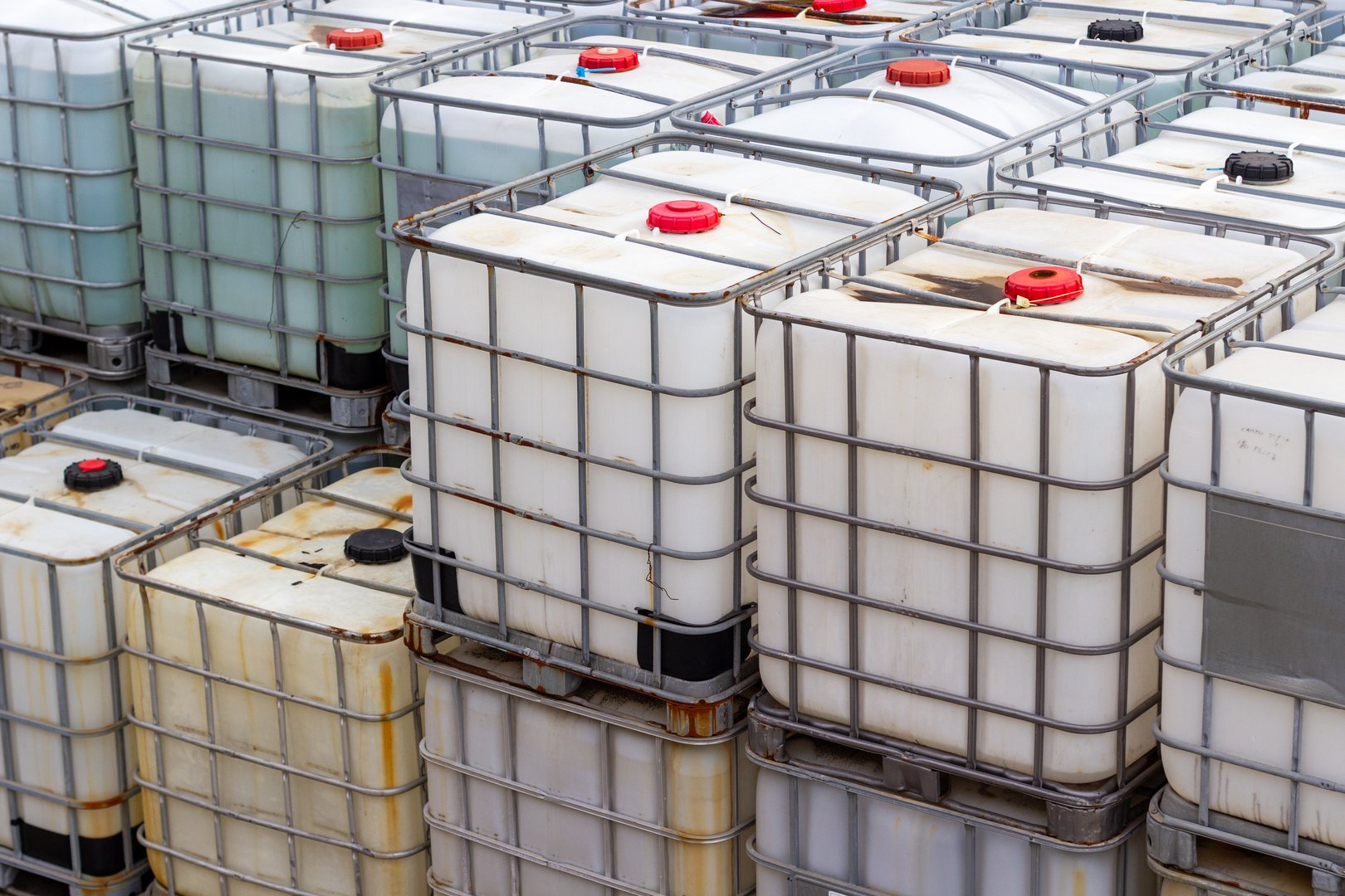 A detailed close-up showcases a stack of industrial bulk containers, specifically IBC totes, arranged in an outdoor setting. These containers, constructed with white plastic interiors and sturdy