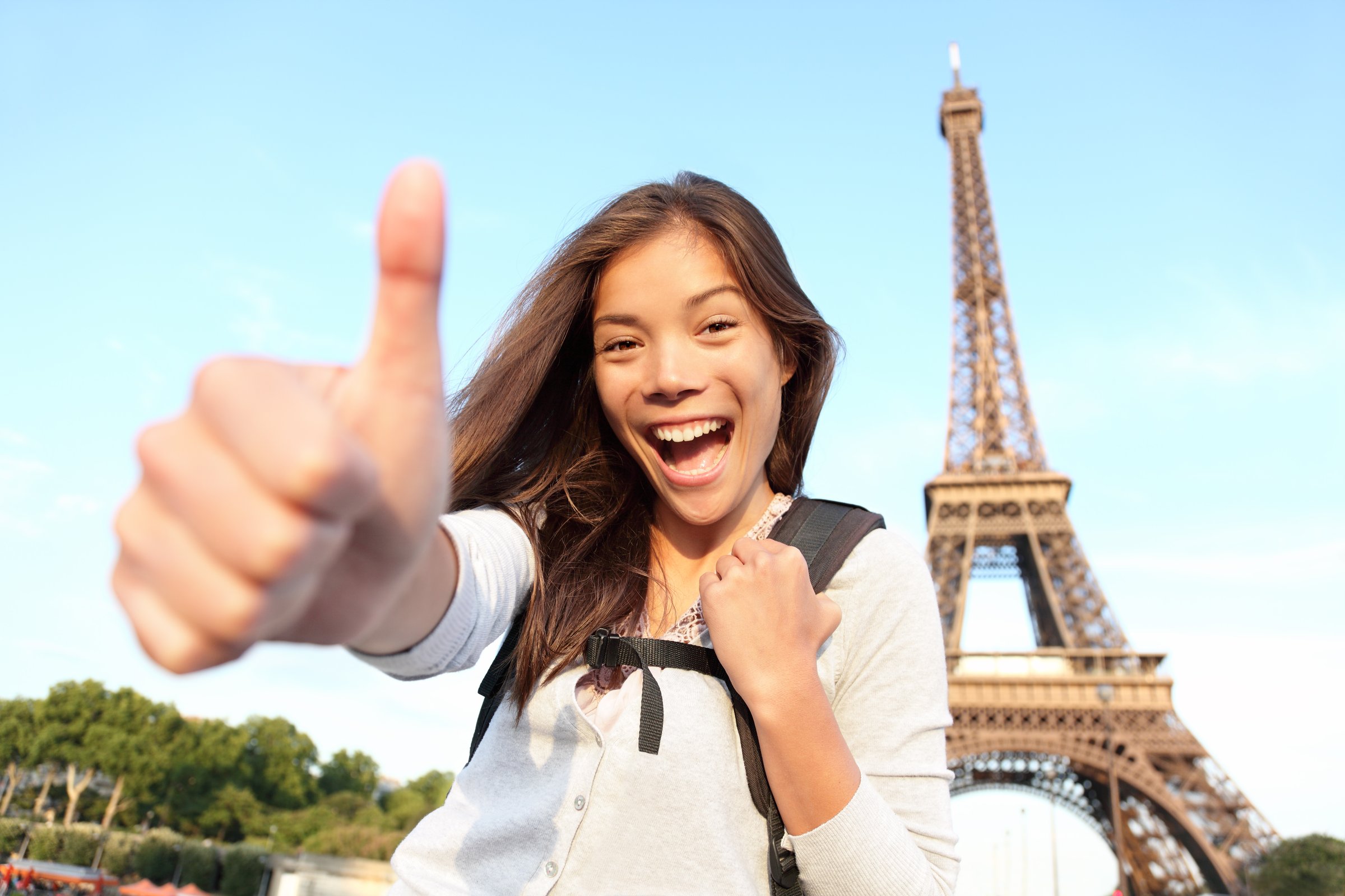 Paris Eiffel tower tourist happy backpacking in Europe. Cheerful smiling woman tourist showing thumbs up success sign in front of Eiffel Tower, Paris. Beautiful Asian Caucasian female model. See more: