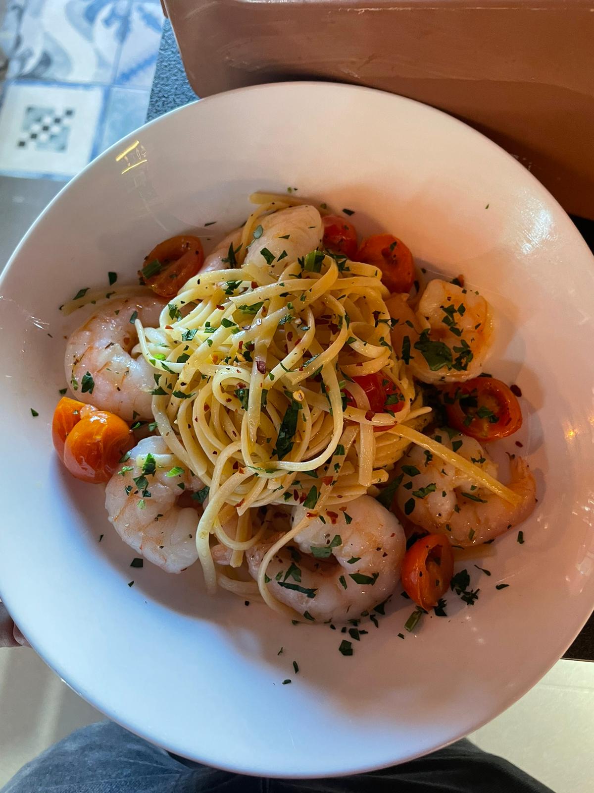 A bowl of spaghetti with shrimp, cherry tomatoes, and herbs, garnished with parsley.
