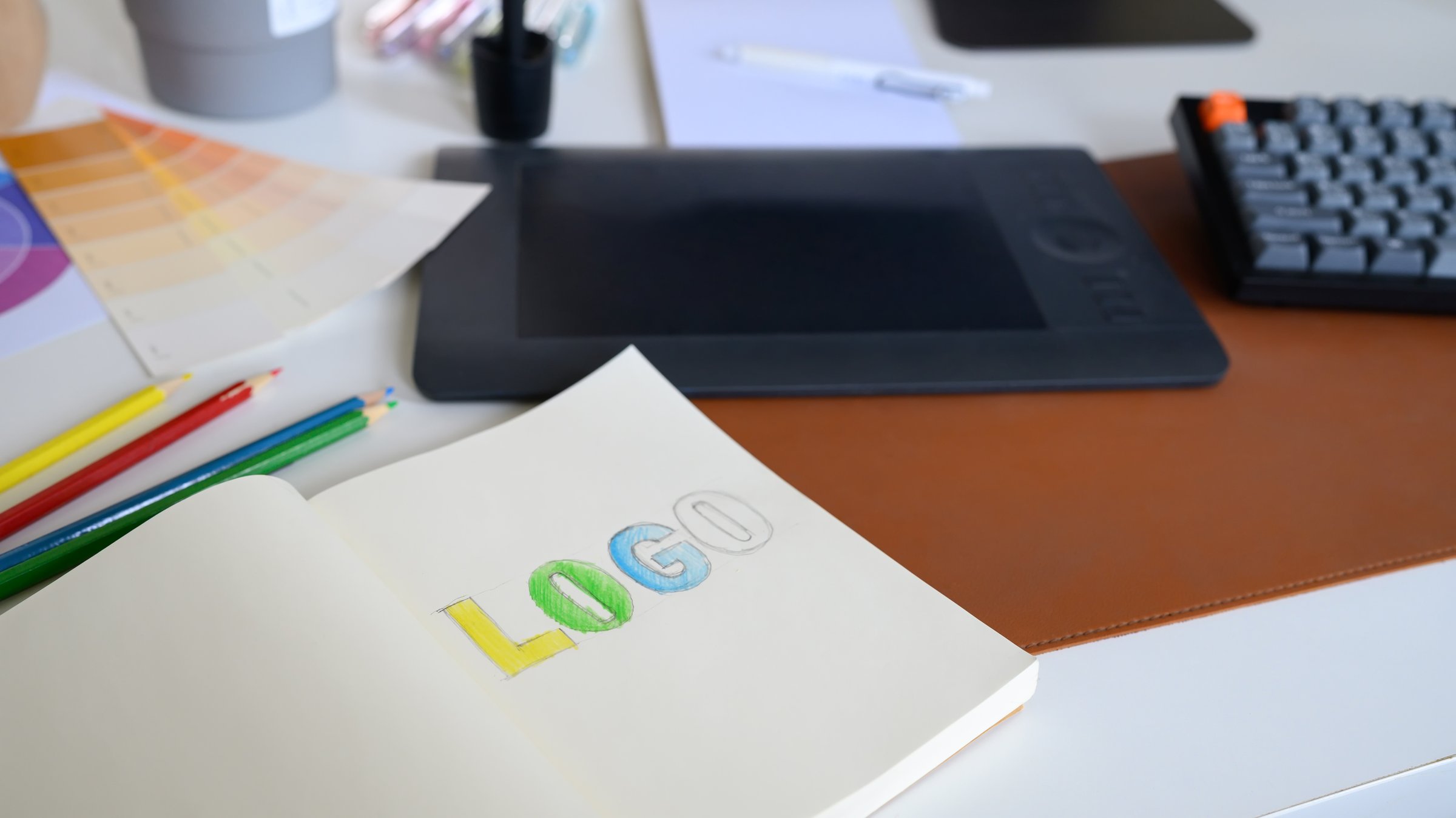 Close-up of logo sketch with color pencils, palette, and tablet on designer workspace in modern creative office.