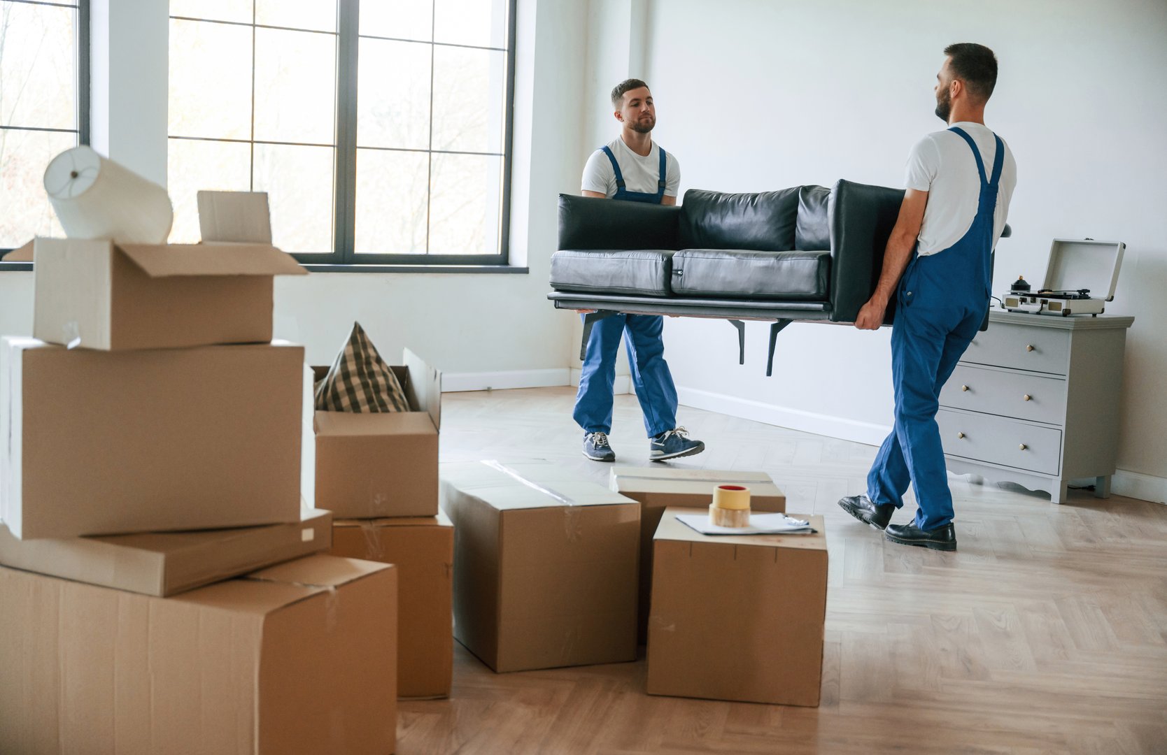Holding heavy sofa. Two moving service employees in a room.
