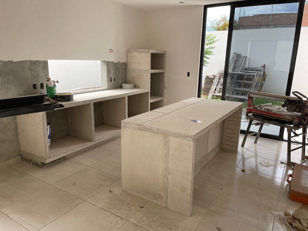 Partially constructed kitchen with concrete island and counters, large glass doors, and tools scattered on the floor.