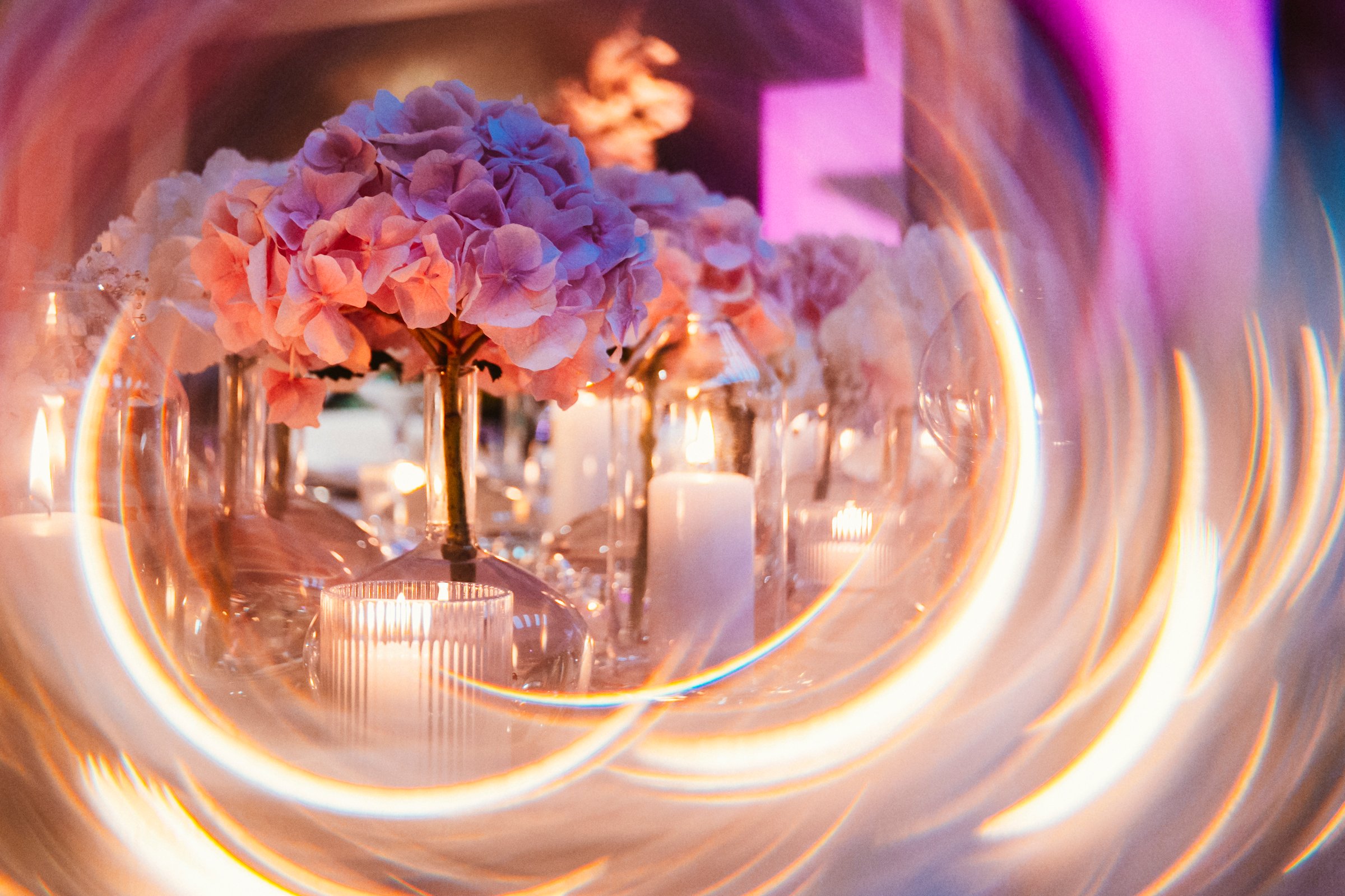 Pink hydrangea flowers arranged elegantly in vases with glowing candles create a romantic atmosphere. Soft lighting enhances the delicate petals, perfect for a wedding or special event
