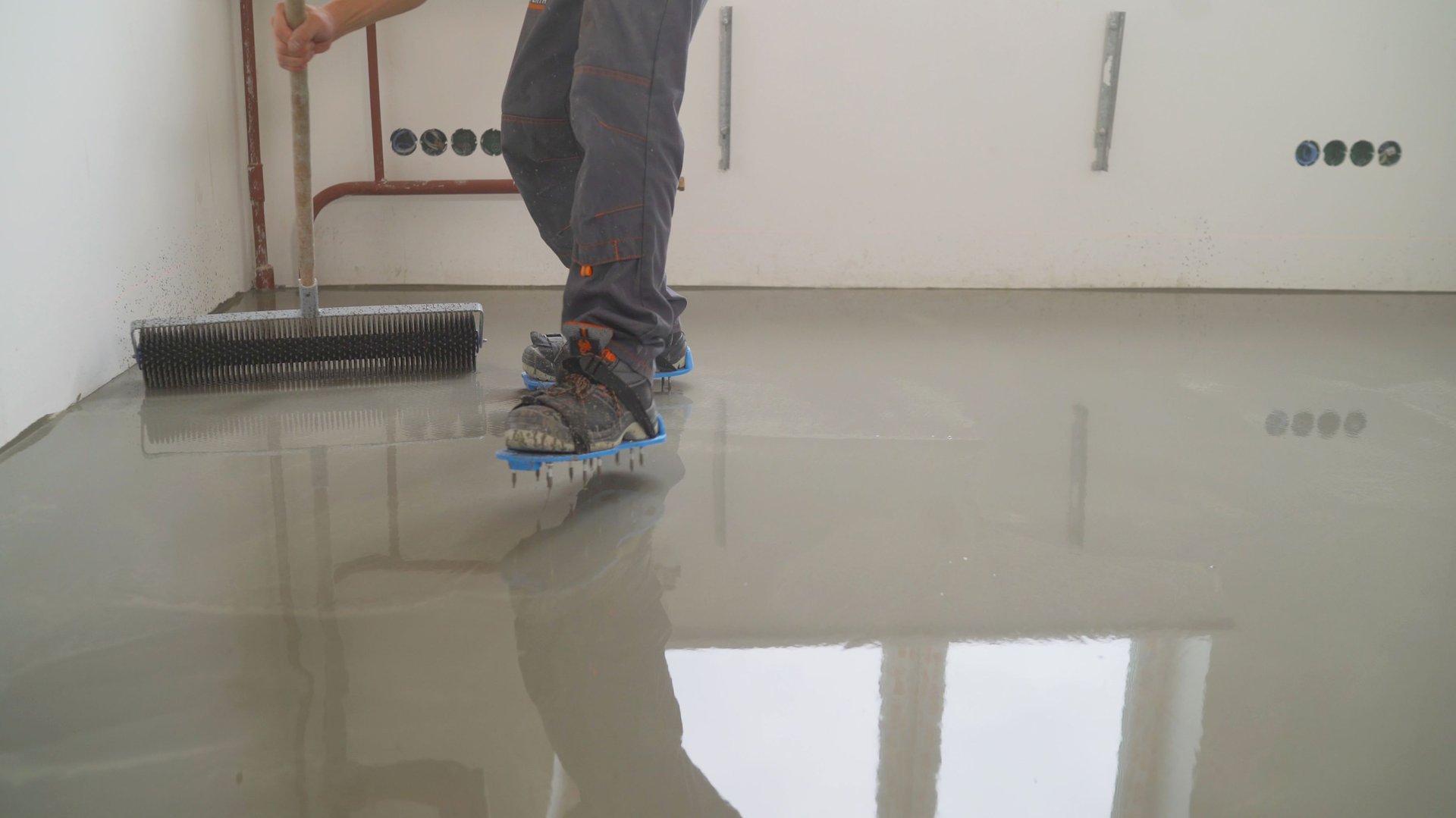 Finishing works - Needle roller for bulk floor. A worker rolls out the liquid floor with a trowel. Squeegee for distributing the mixture. The worker levels the liquid floor.