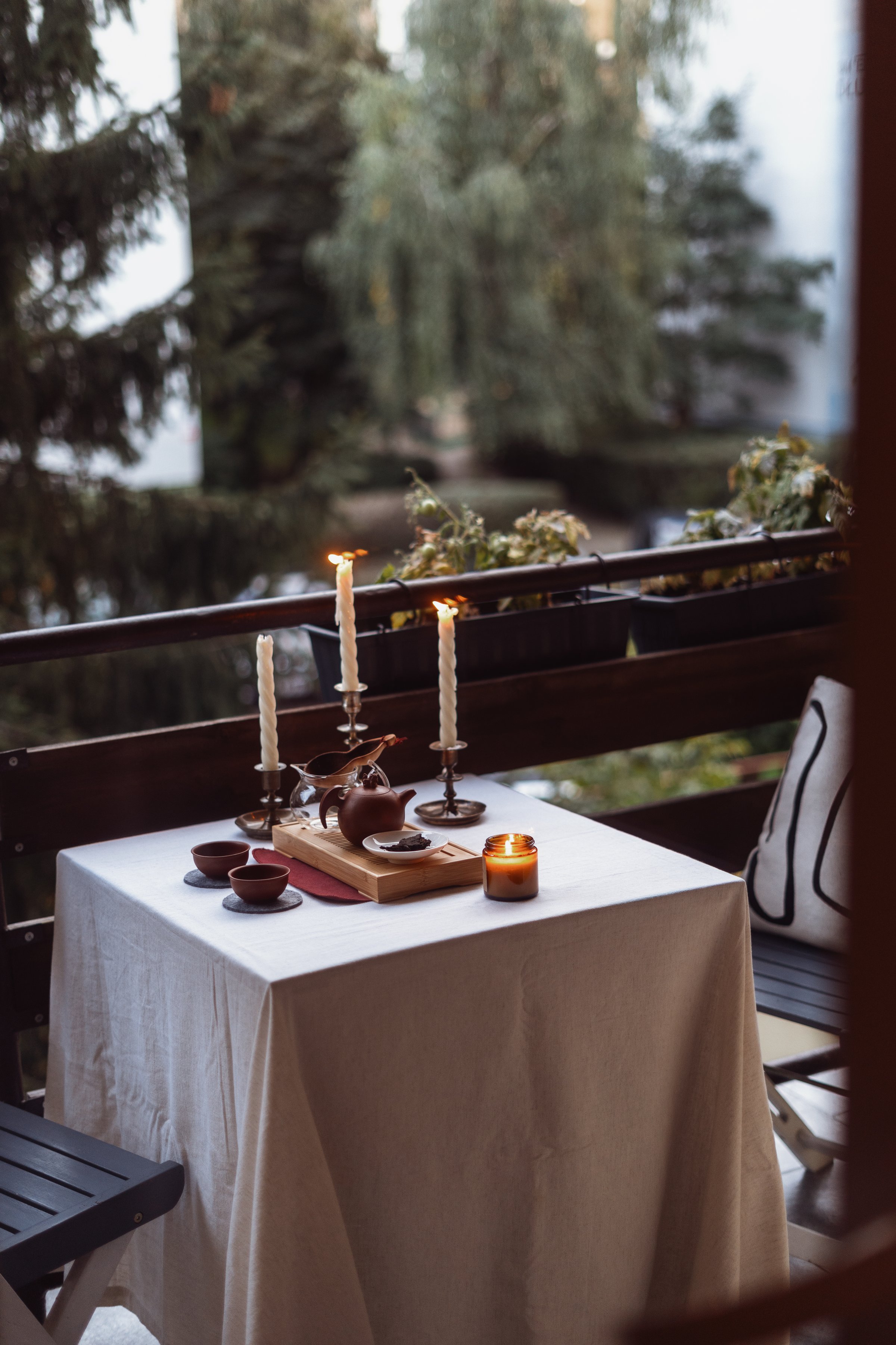 Enjoy a serene autumn evening on the balcony, featuring a traditional chinese set for tea on table with small clay cups, teapot and candles lights, creating a warm, inviting and relaxation atmosphere