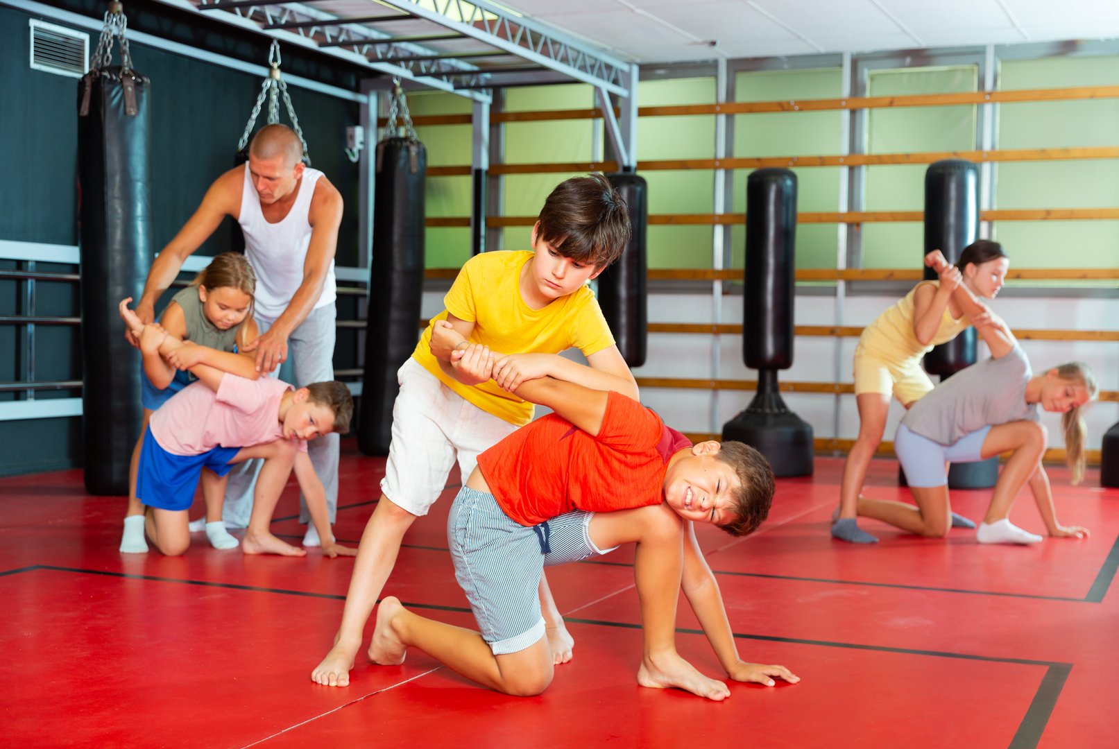 Sportive preteen kids practicing in pair self-protection in class with teacher