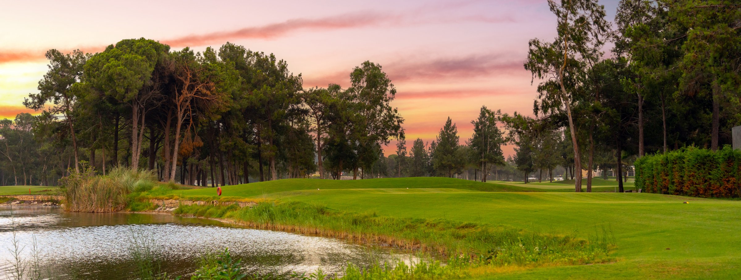 A tranquil golf course with a reflective pond and lush greenery, set against the soft pastel hues of a peaceful sunset