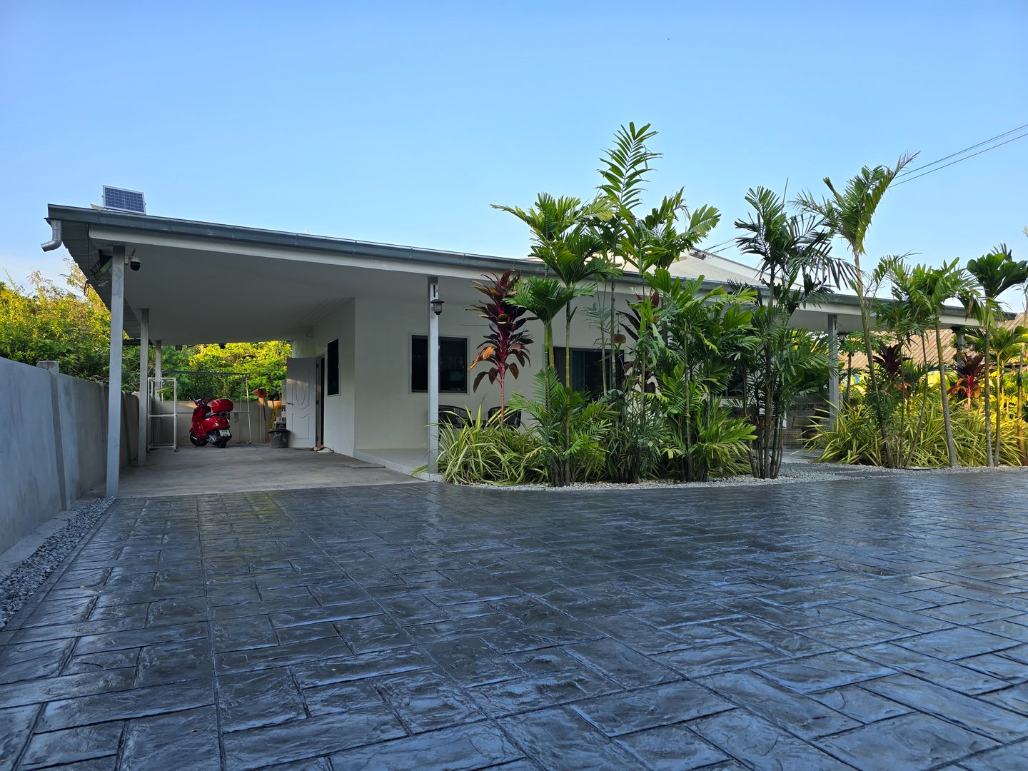 This striking modern home features an exquisite stamped concrete driveway, surrounded by lush greenery, in the vibrant city of Pattaya, Thailand, a Thai Suburban area with a modern family house