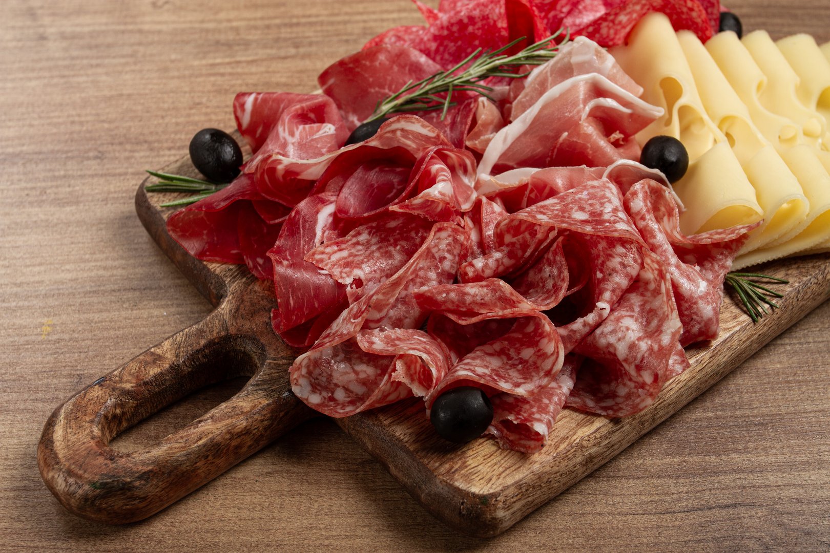 Assorted meat, appetizer, prosciutto, salami and ham, with maasdam cheese and olives, on a wooden board, breakfast, top view, close-up, no people