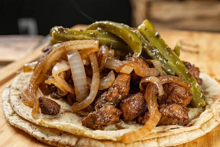 Taco with grilled beef, sautéed onions, and green peppers on a wooden surface.