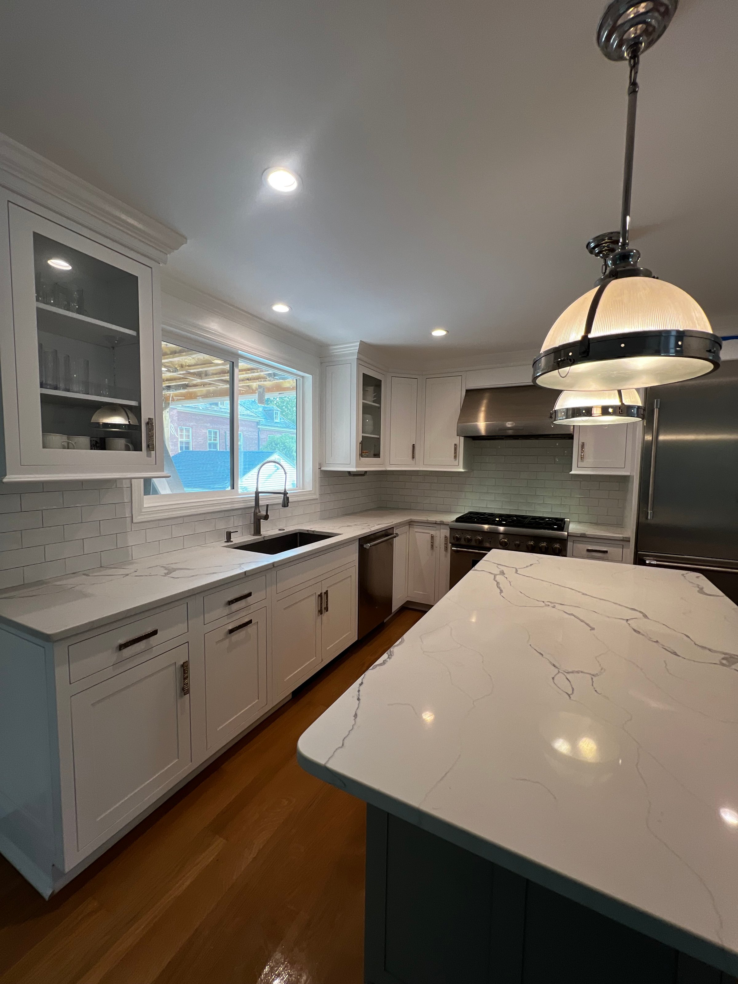 A kitchen detail with white cabinets and square tile backsplash, a waterfall marble countertop and wood slat panel front, and a gold light fixture, hardware, and faucet. No brands or labels.