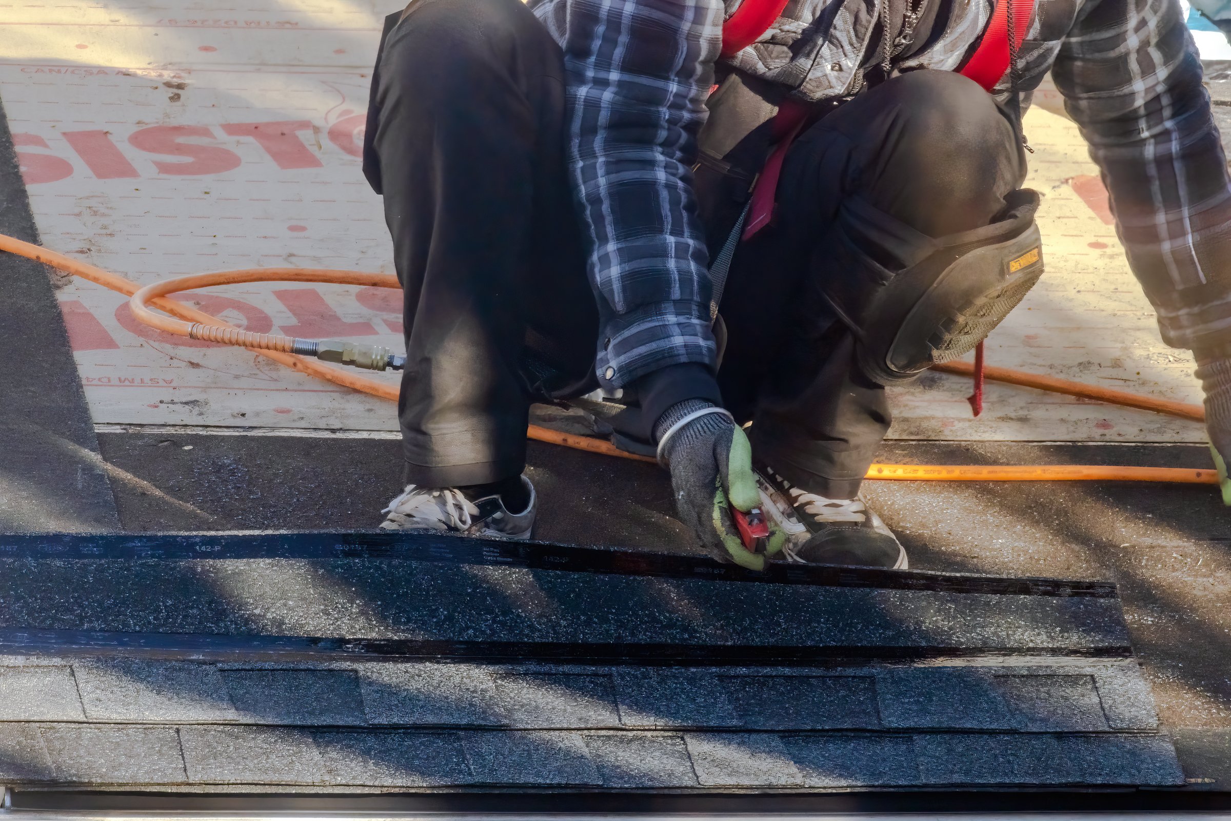 Calgary, Alberta, Canada. Oct 23, 2024. A worker, wearing safety gear and gloves, crouches on a roof while using a pneumatic nail gun to install roofing materials with precision.