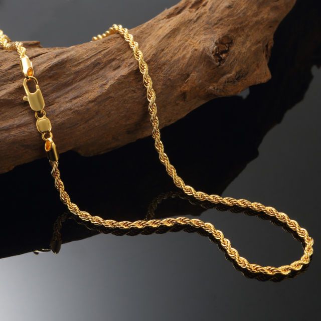 Gold rope chain necklace with a lobster clasp displayed on a piece of driftwood against a black background.