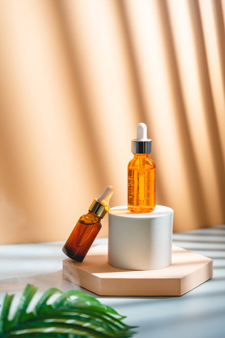 Glass cosmetic bottle with oil or serum for skin care on special podium on apricot color background. Natural skin care concept. Harsh shadows