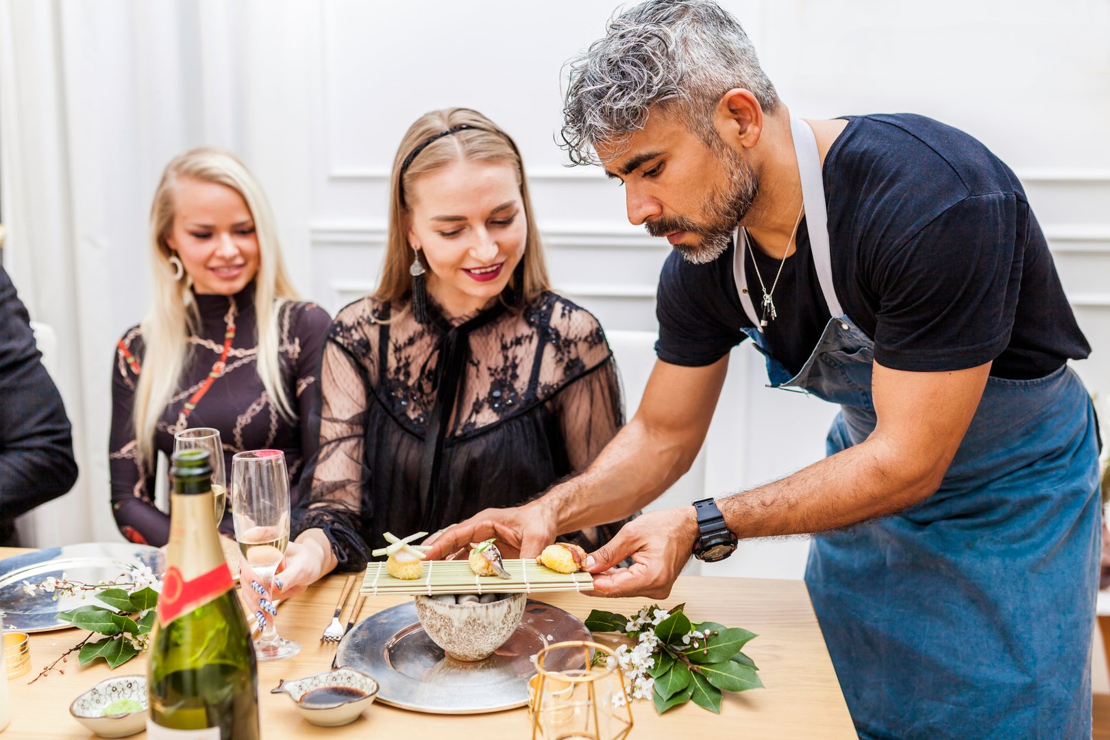 Latin cook serving food to clients at table during private dinner at home. Chef serving sushi to stylish group of people.