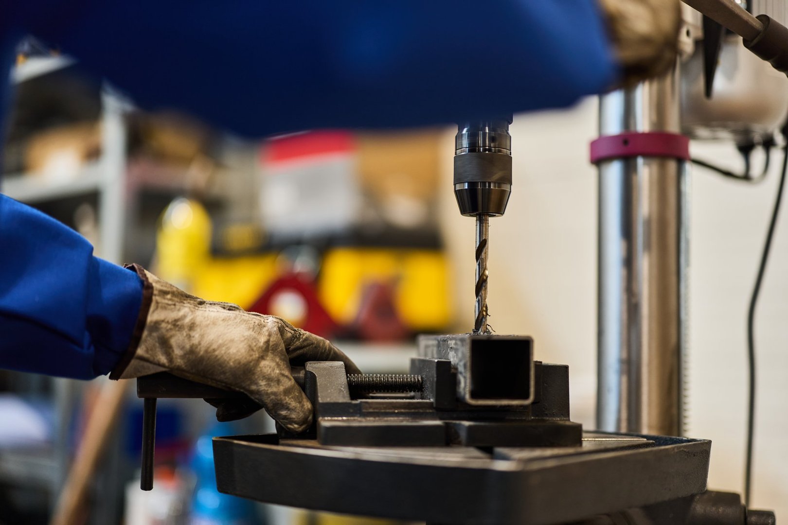 Metal drilling process with drill press and worker in protective gear in workshop