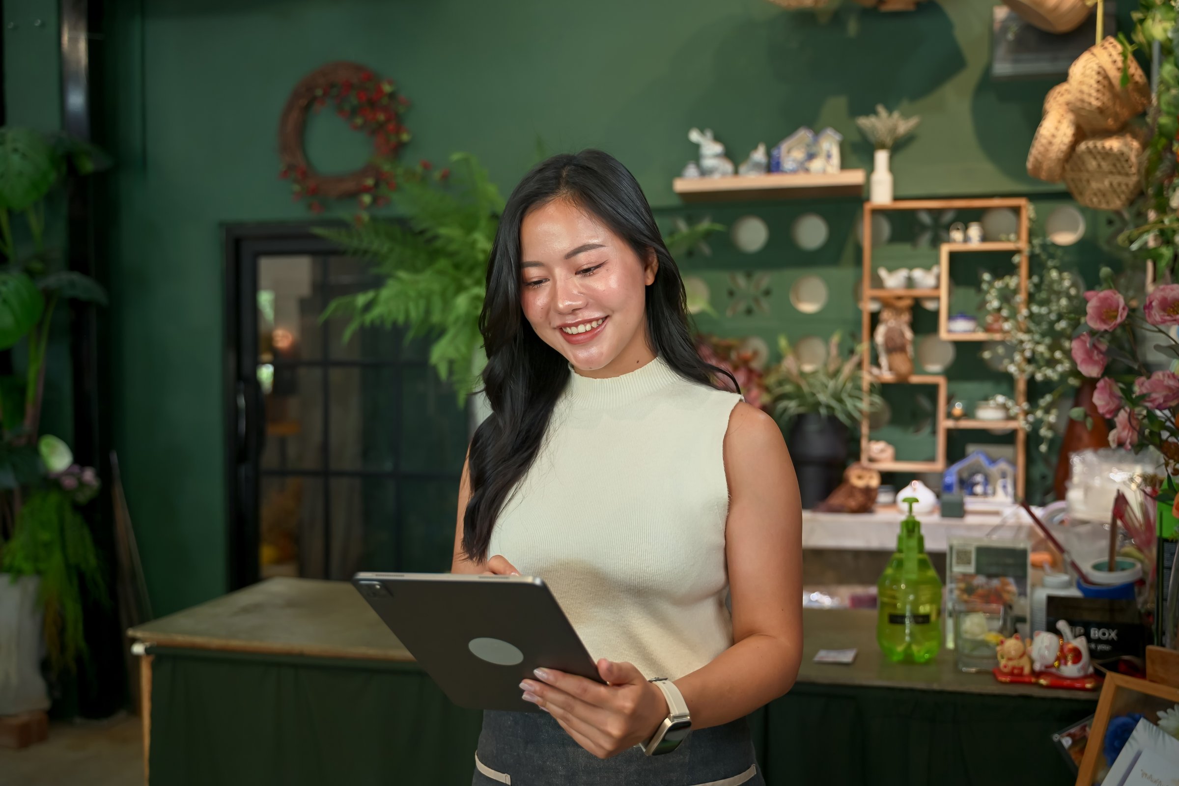 Florist woman checking customer orders on digital tablet inside flower shop.