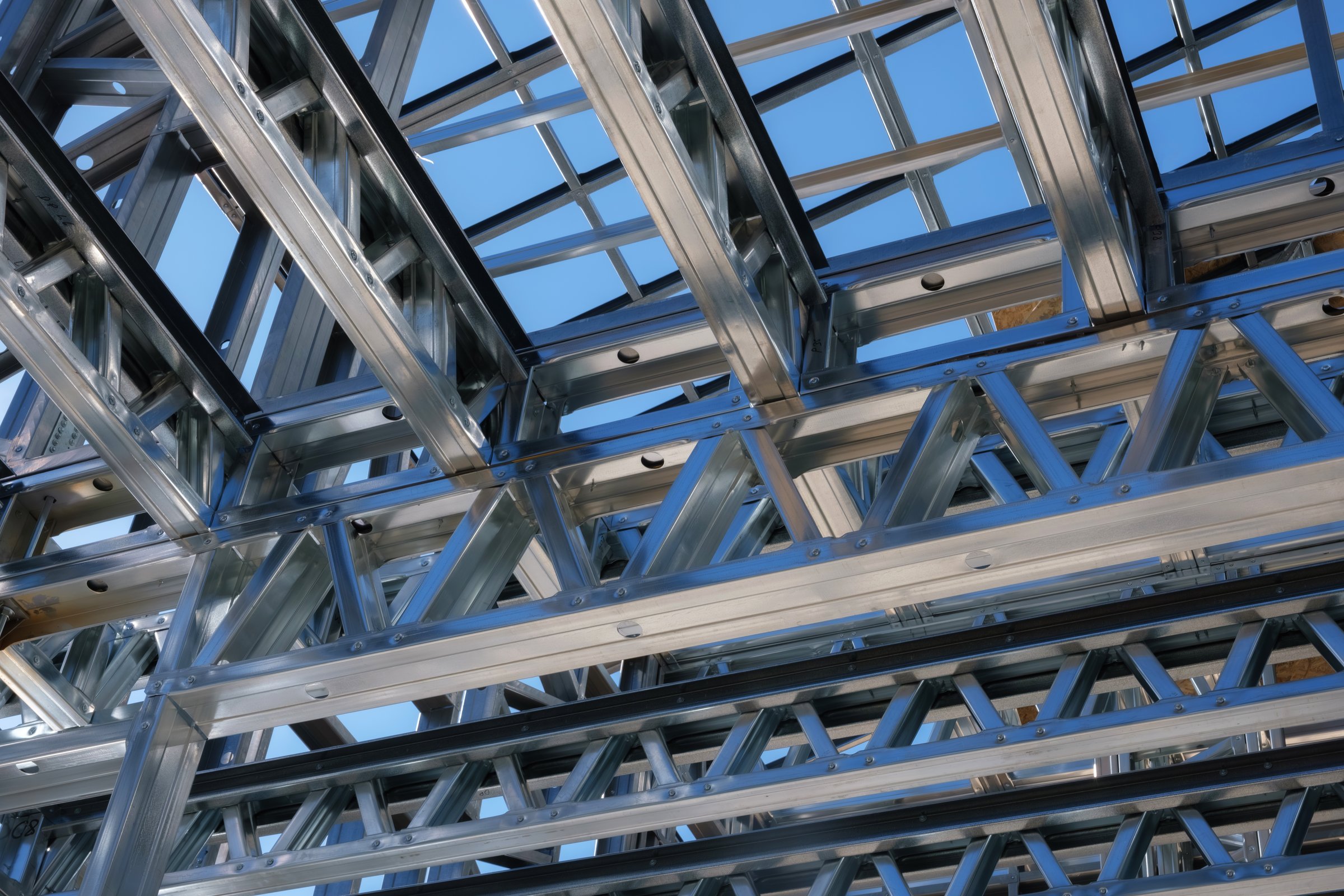 Close-up view of a steel frame structure under construction with a clear blue sky in the background. Modern architecture showcasing metal trusses and industrial design elements.