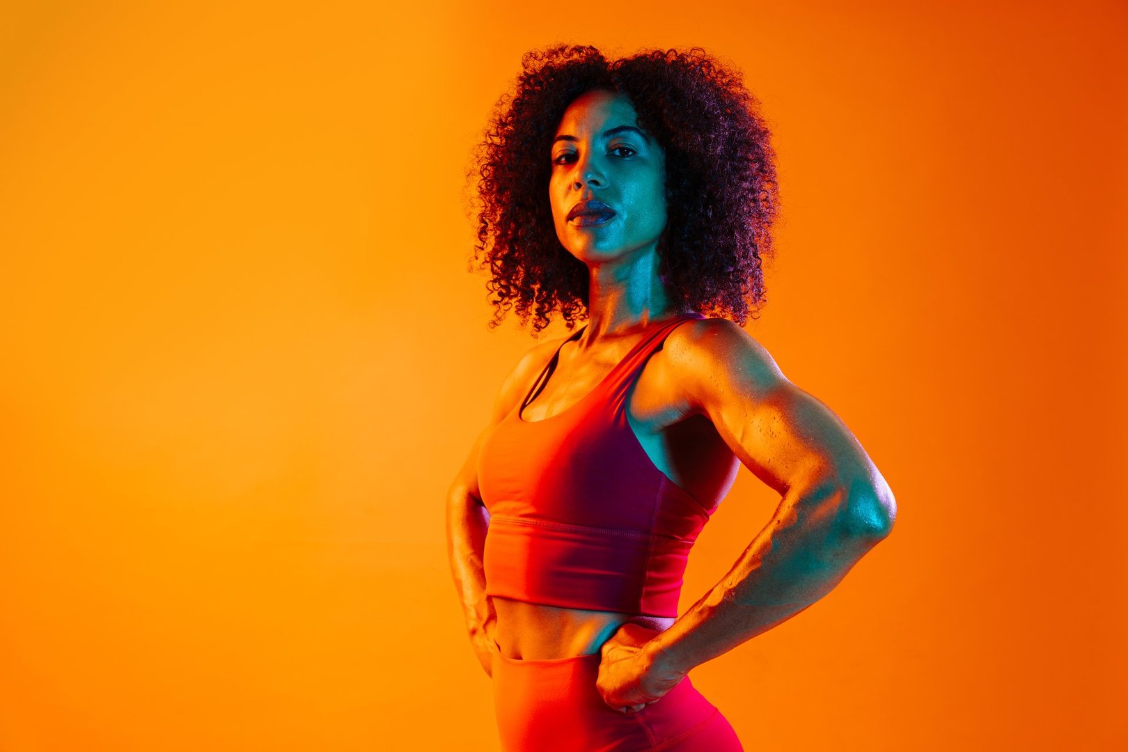 Sportive black hispanic woman wearing sportswear training in fitness studio, colorful dramatic lighting - African-american female athlete doing sport workout