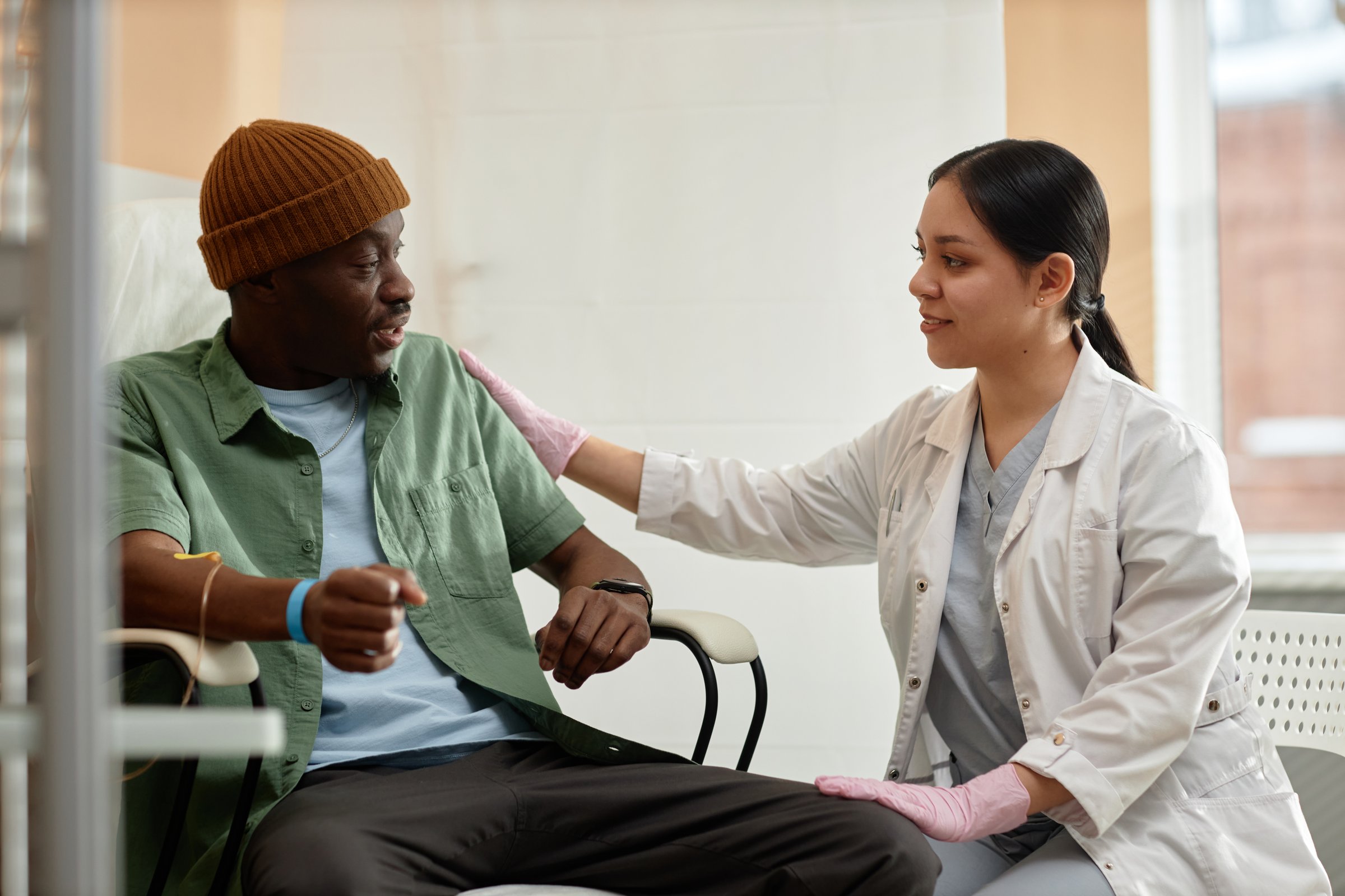 Side view portrait of smiling female doctor comforting patient receiving IV treatment in clinic