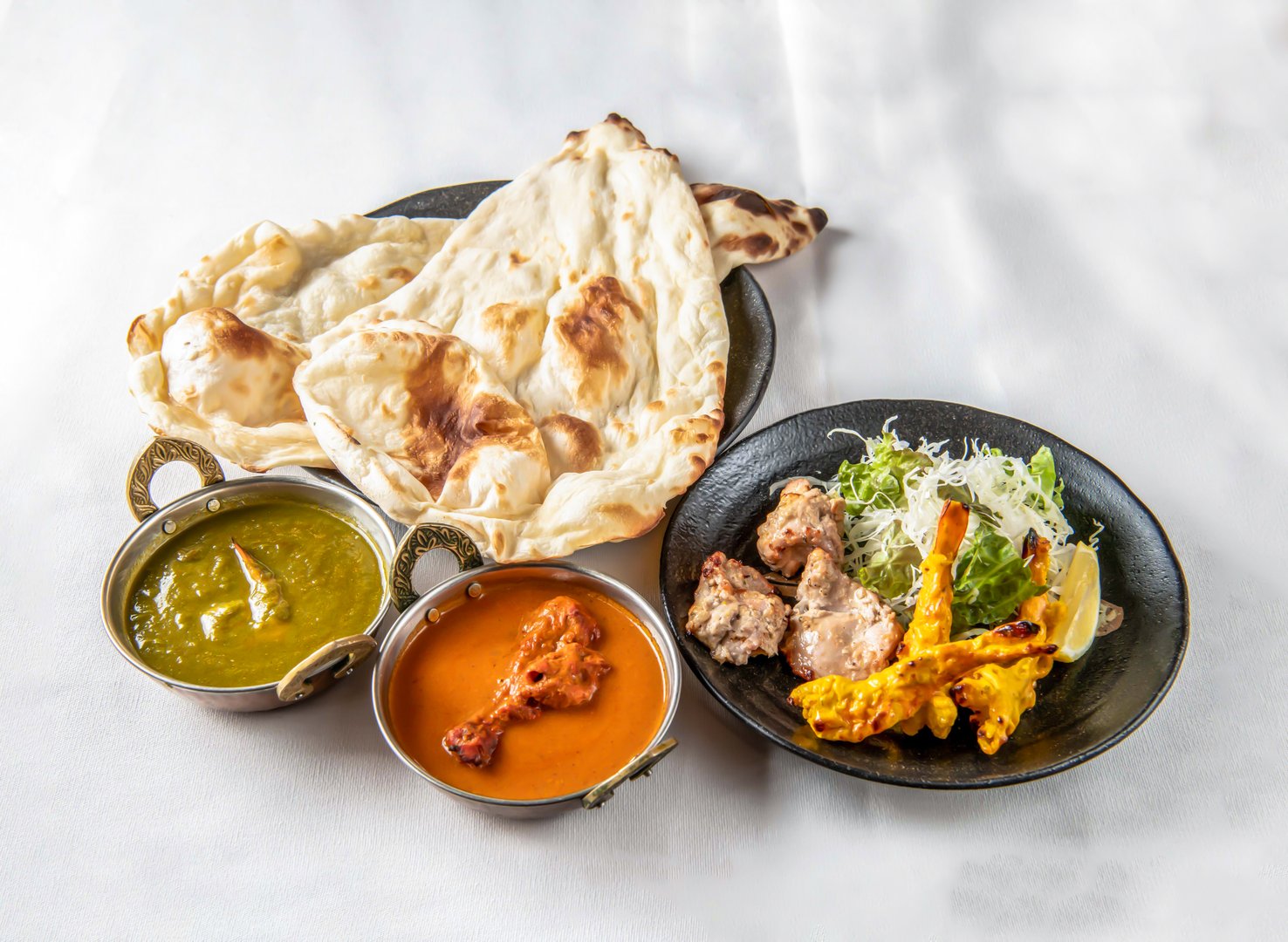 Indian Curry Set with Saag Curry, Chicken Curry, Naan, Tandoori Chicken and Chicken Tikka on a White background side view of indian food