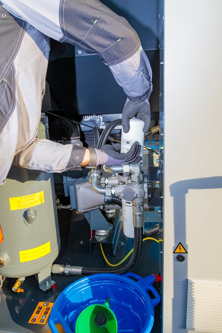 Technician replacing oil filter in industrial air compressor during maintenance