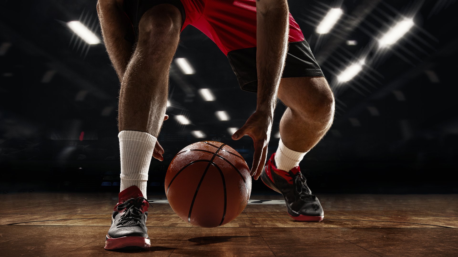 Basketball player dribbling the ball on a hardwood 3D court during a game, captured from a low angle with focus on the legs, shoes, and bouncing ball. Concept of strategy, focus